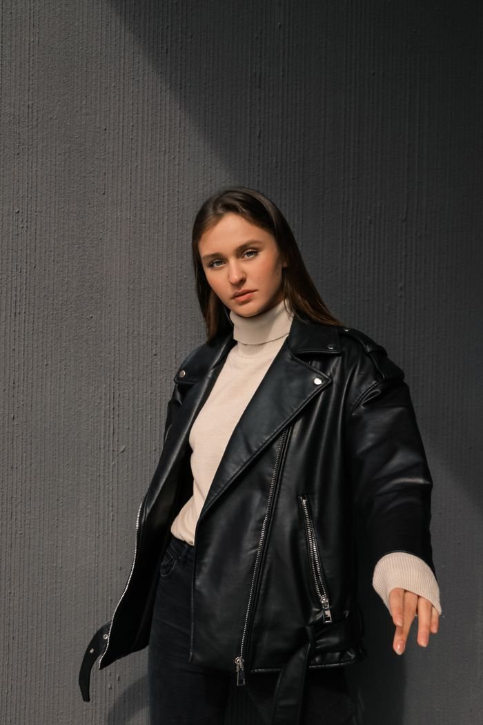 Young woman posing confidently in a black leather jacket and turtleneck sweater.