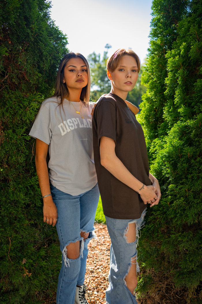 Two young women pose in casual outfits surrounded by greenery, exuding a fresh and trendy vibe.
